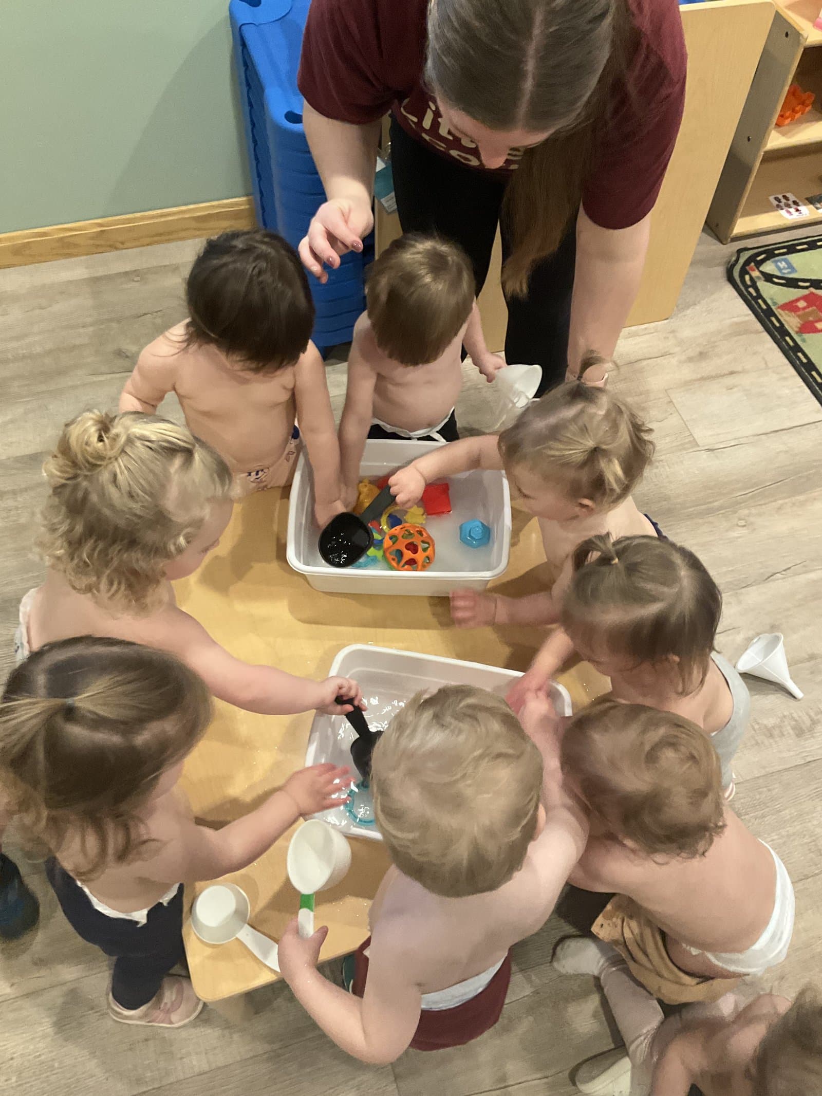 Sprouts classroom toddlers around a sensory water table with their teacher