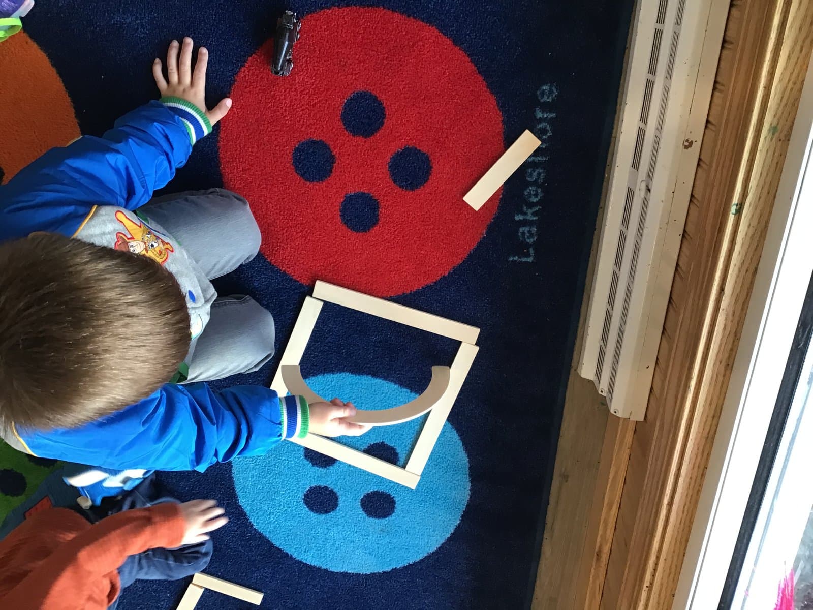 Little Acorns classroom — children learning with wooden blocks on a colorful rug