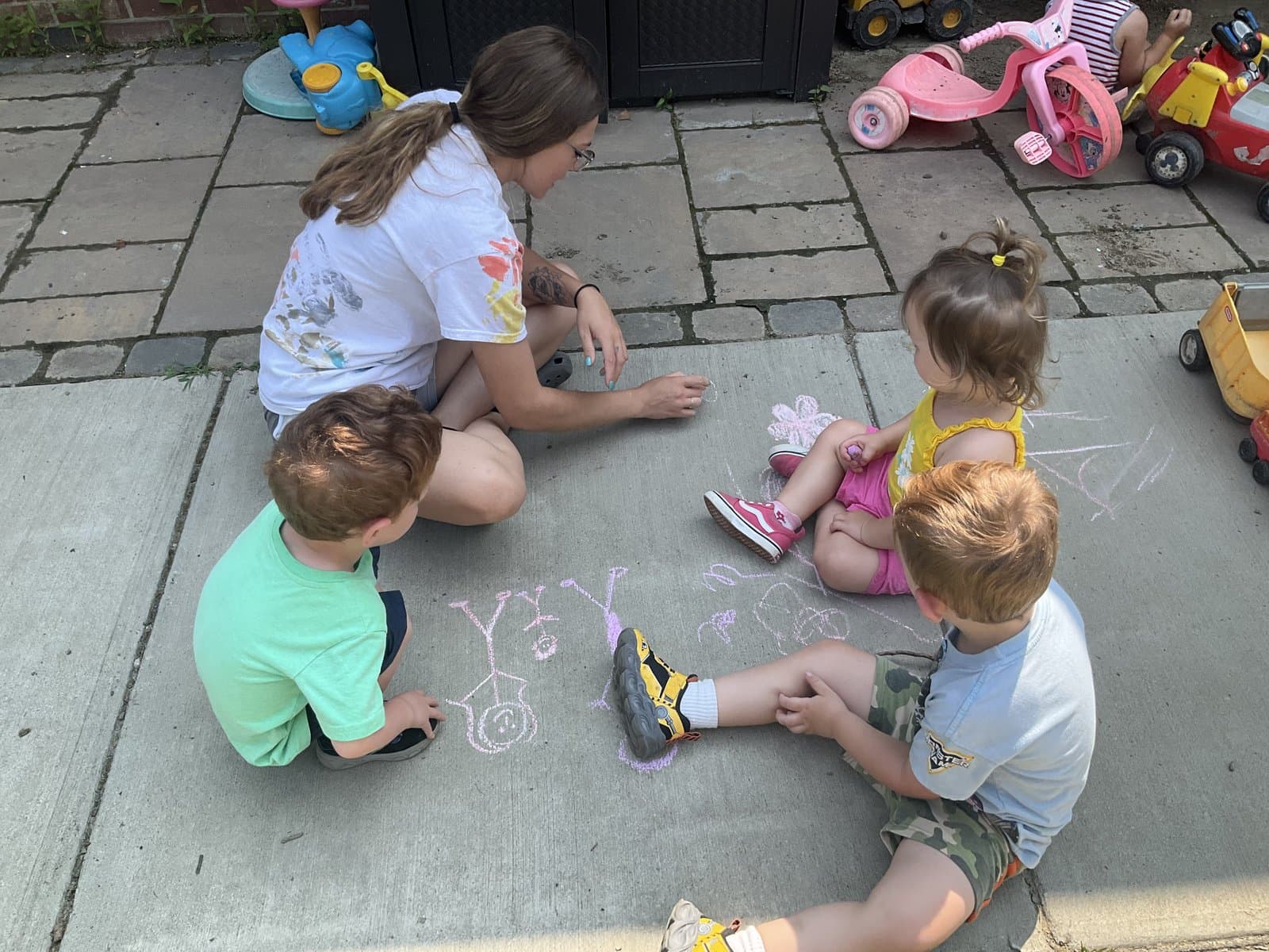 Little Acorns playground — teacher and three children drawing with sidewalk chalk