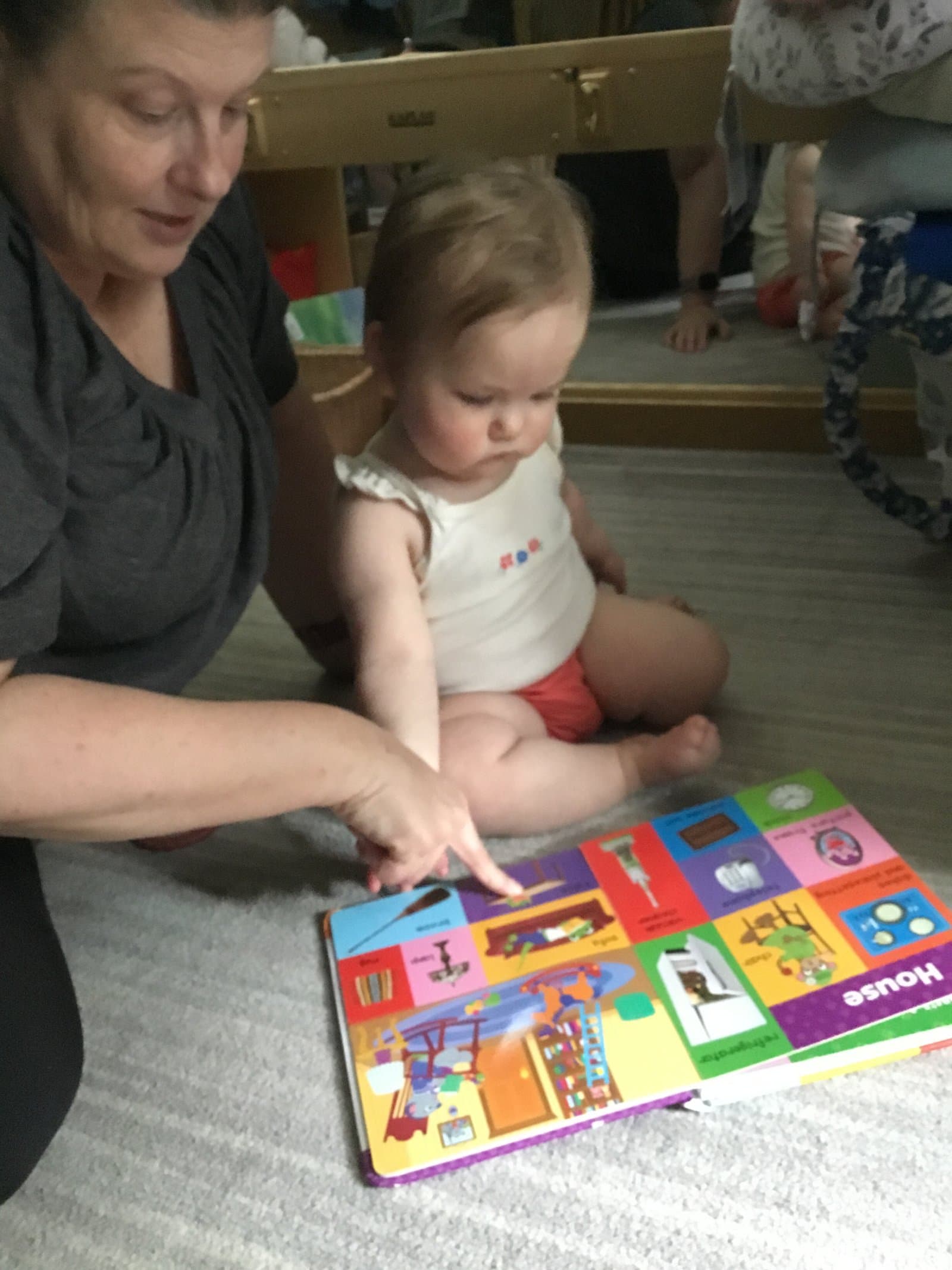 Little Acorns nursery teacher reading a picture book with an infant